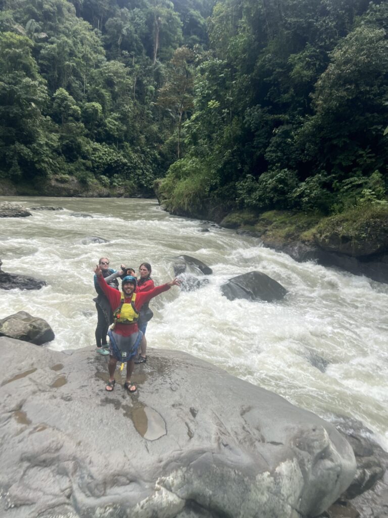 Three paddlers cheer from a huge boulder beside a powerful rapid in a jungle river canyon