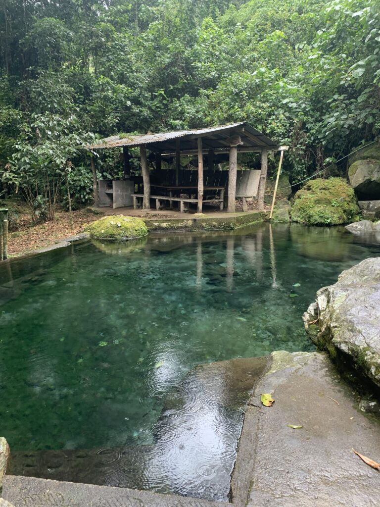 A clear, spring-fed green pool and a rustic open-sided shelter in the forest at Cachí