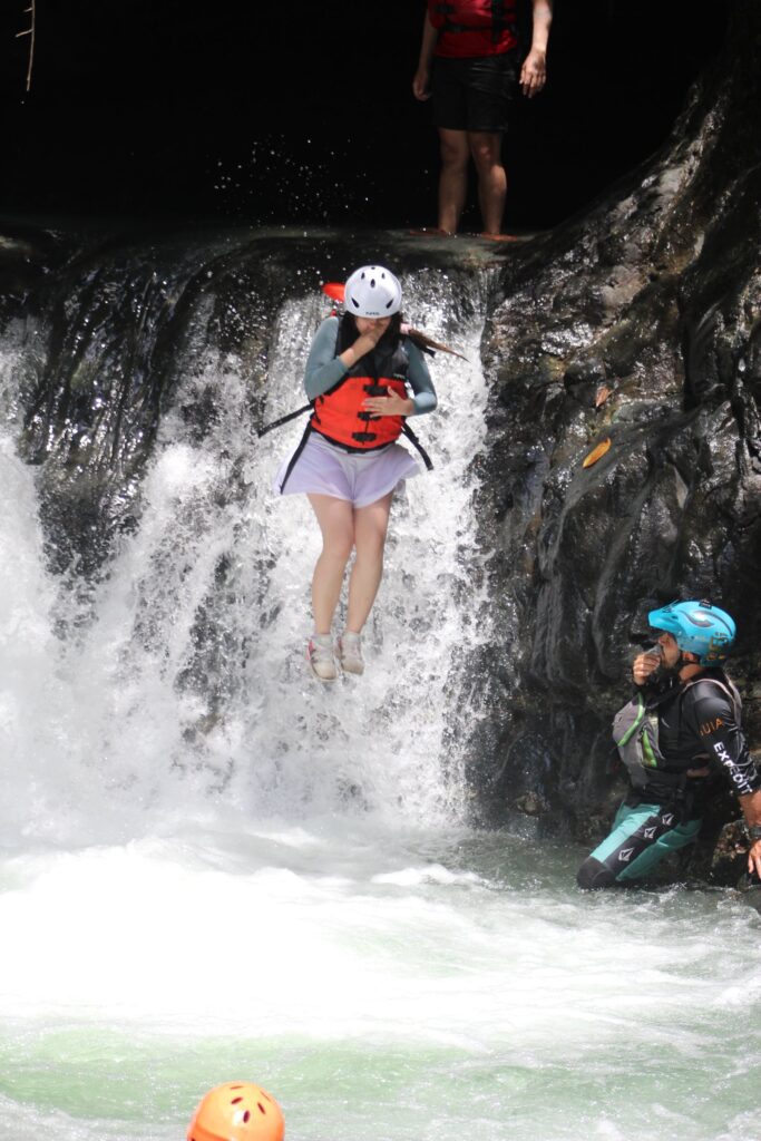 A rafter in a helmet and life jacket jumps from the lip of a jungle waterfall while a guide waits in the pool below