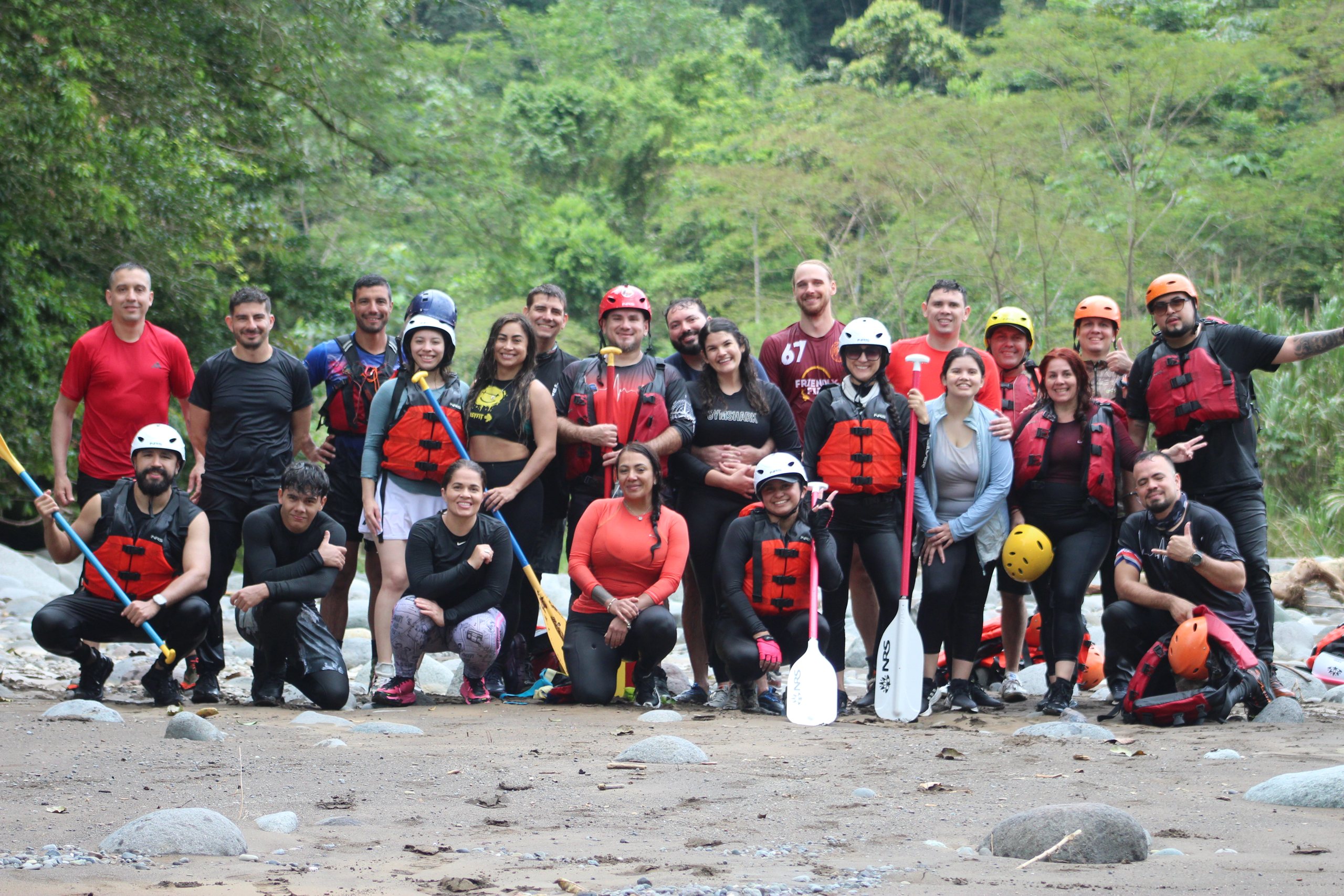 A big group of rafters and guides in life jackets and helmets on a stony beach beside the Pacuare River