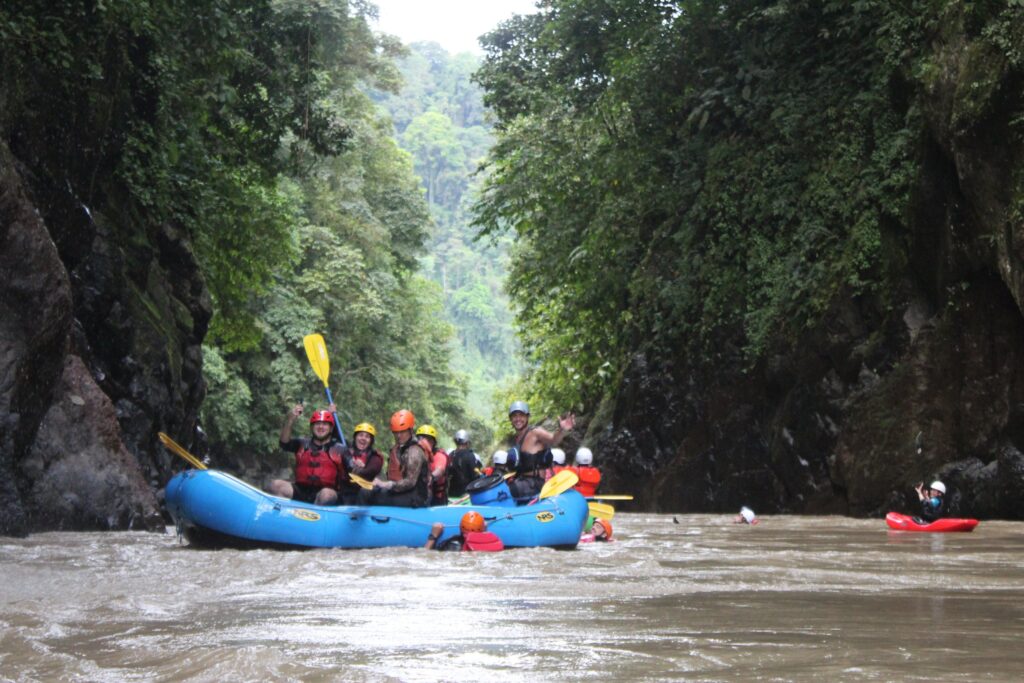 A raft and a safety kayaker float through the Pacuare's steep jungle gorge, cliffs and rainforest rising on both sides