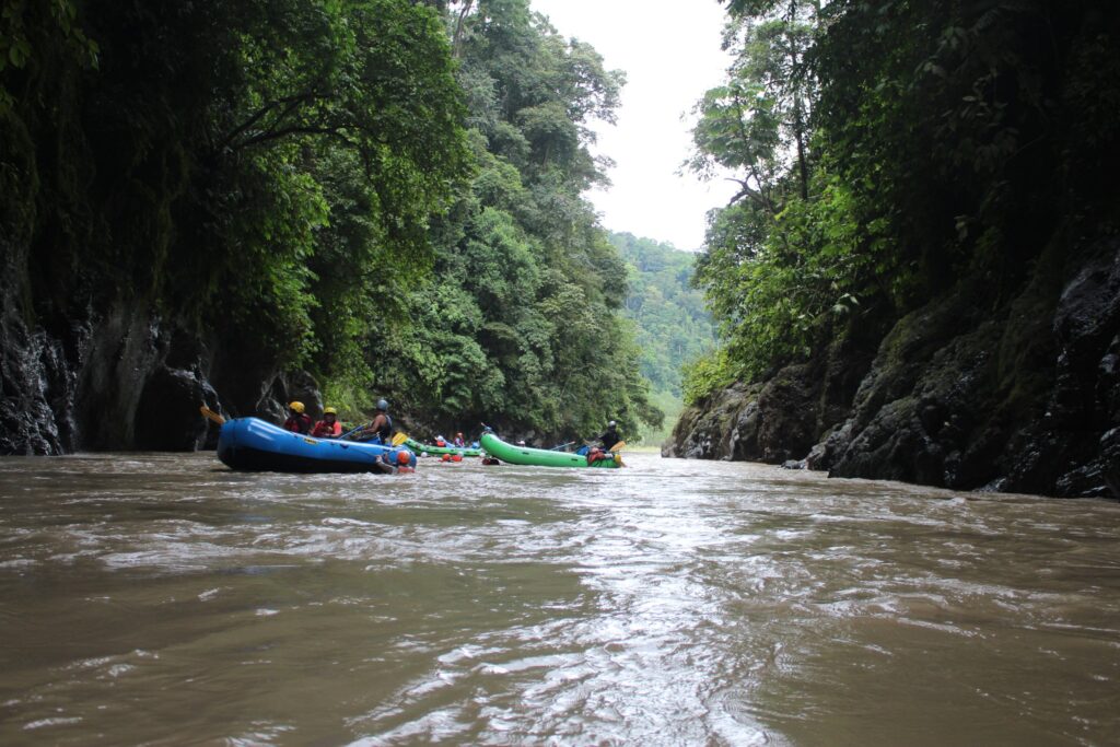 Blue and green rafts drift in a line between sheer, jungle-covered canyon walls on a calm stretch of the Pacuare